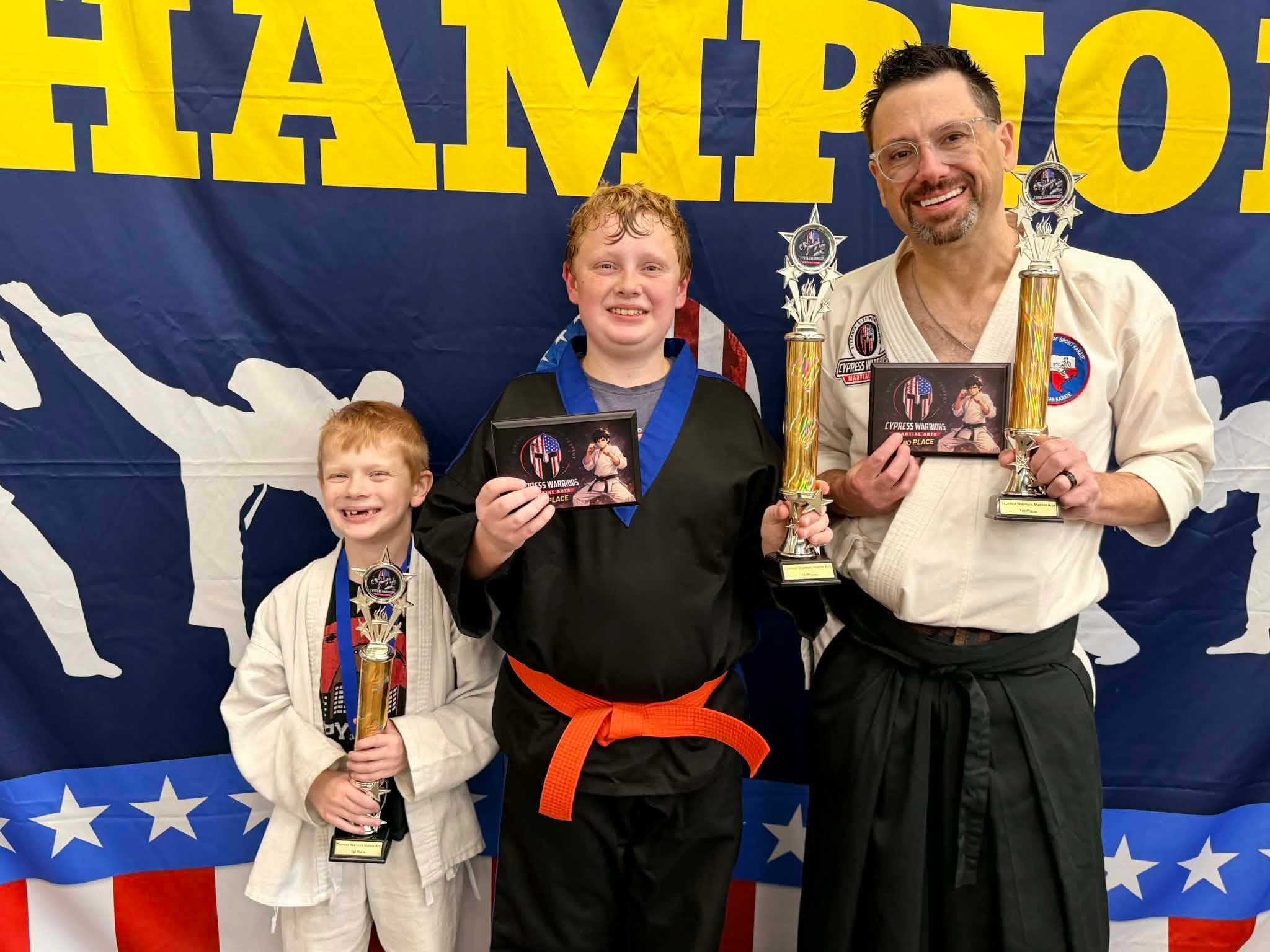Three karate competitors standing together with trophies and awards.