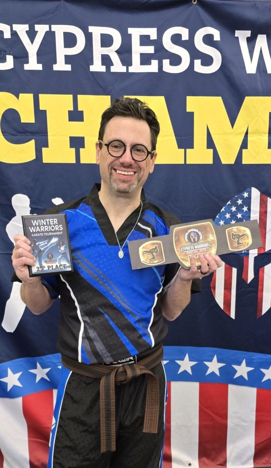 A competitor in a blue and black martial arts uniform holding tournament awards.