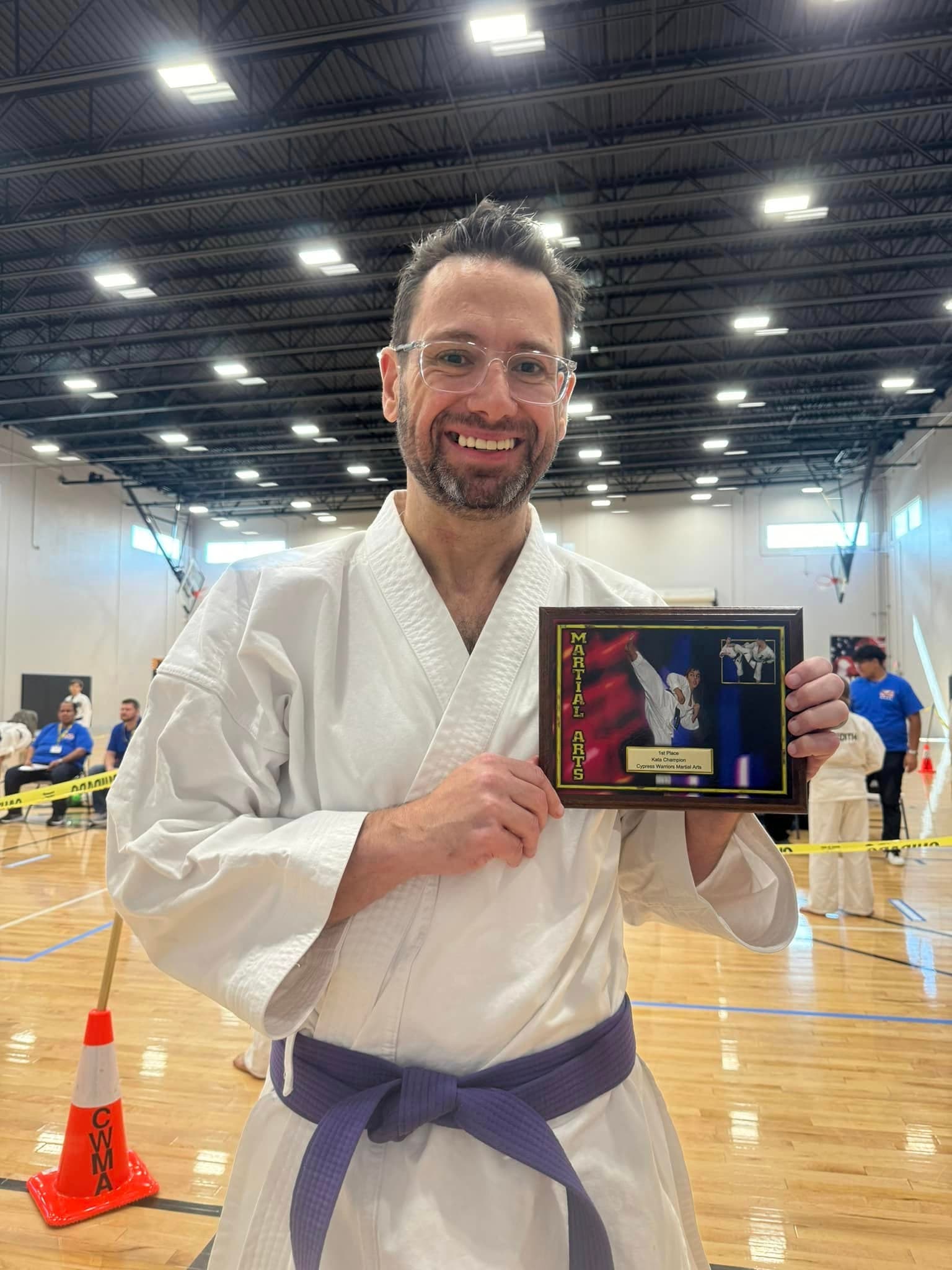 A karate competitor wearing a purple belt and holding a framed award.